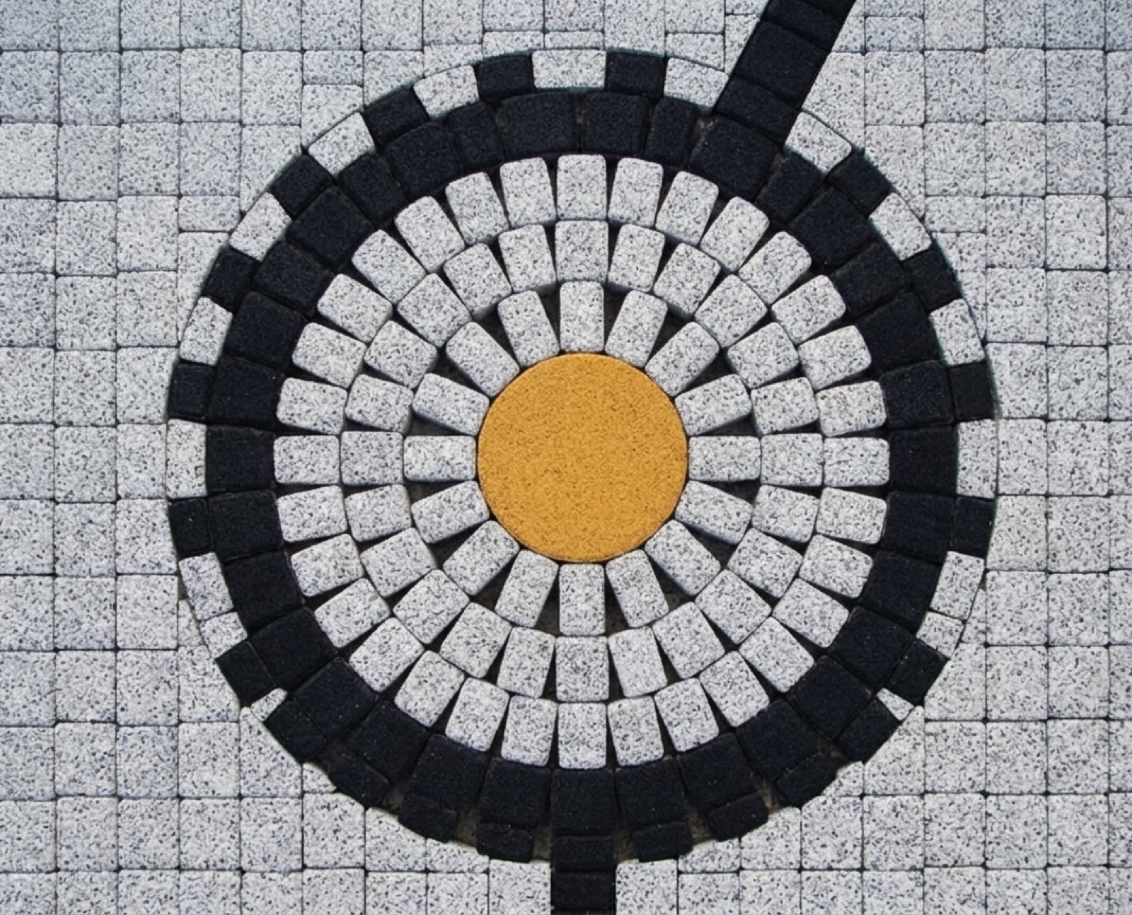 ANTIK circular cobble medallion — yellow centre and white rings set in a grey cobble field
